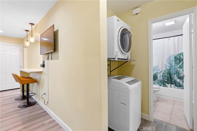 laundry room featuring light wood-type flooring, laundry area, baseboards, and stacked washer / drying machine