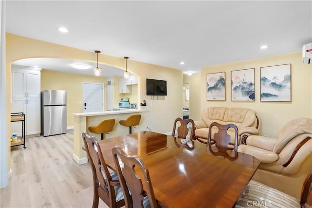 dining space featuring arched walkways, baseboards, light wood-style flooring, and recessed lighting