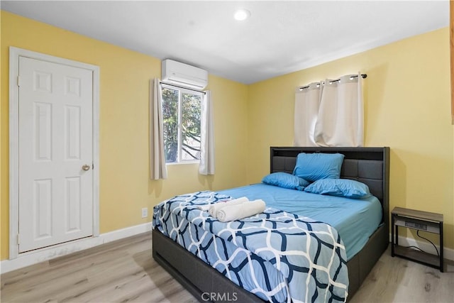 bedroom featuring a wall mounted air conditioner, baseboards, and wood finished floors