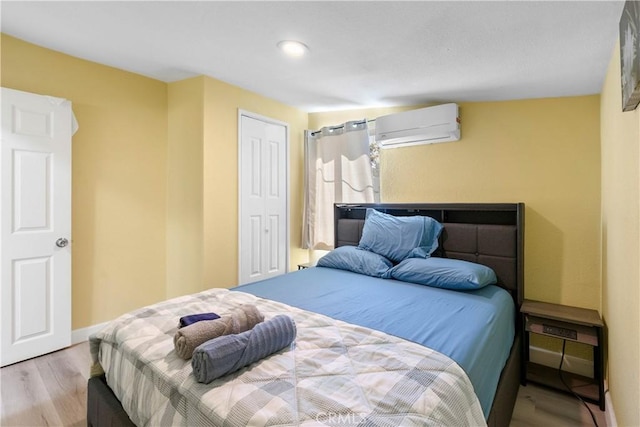 bedroom with a wall unit AC, a closet, baseboards, and wood finished floors