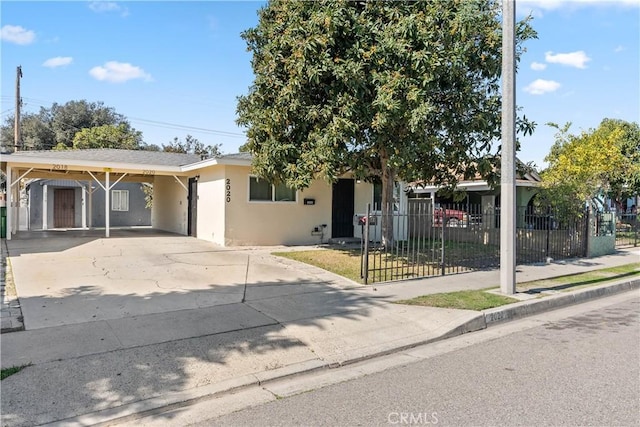 ranch-style home with driveway, a fenced front yard, a carport, and stucco siding