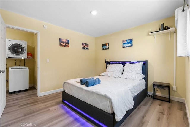 bedroom featuring stacked washing maching and dryer, light wood-style flooring, and baseboards