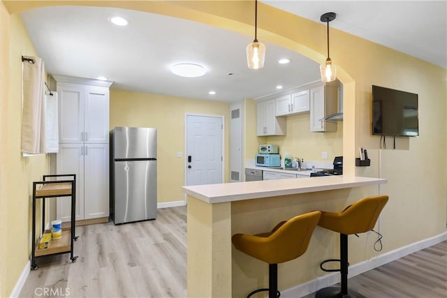 kitchen with white microwave, light wood-style floors, freestanding refrigerator, a peninsula, and a kitchen bar