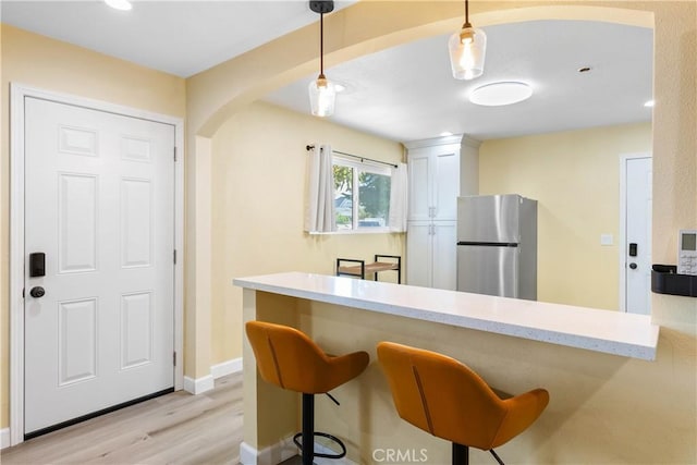 kitchen featuring arched walkways, white cabinets, freestanding refrigerator, a kitchen bar, and pendant lighting