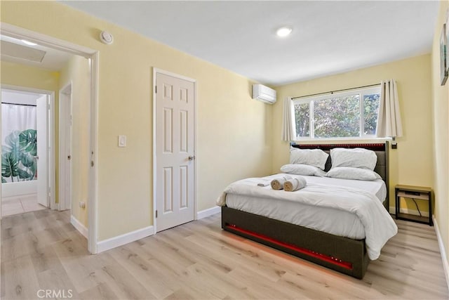 bedroom with light wood finished floors, a wall mounted air conditioner, attic access, and baseboards