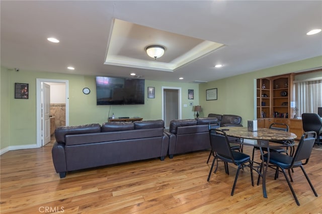 dining area with a raised ceiling, light wood-style flooring, and recessed lighting