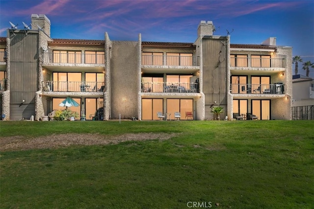 back of property at dusk with a lawn and stucco siding