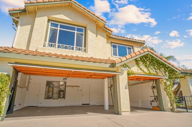 rear view of house featuring a garage, driveway, a tiled roof, and stucco siding