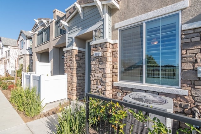 view of home's exterior featuring central air condition unit, stone siding, fence, and stucco siding