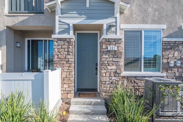 doorway to property featuring stone siding, central air condition unit, and stucco siding