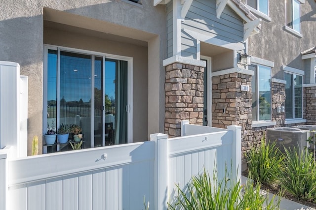 view of property exterior with stone siding, fence, central AC unit, and stucco siding