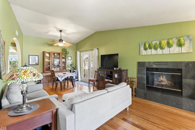 living area featuring ceiling fan, vaulted ceiling, a tiled fireplace, and wood finished floors