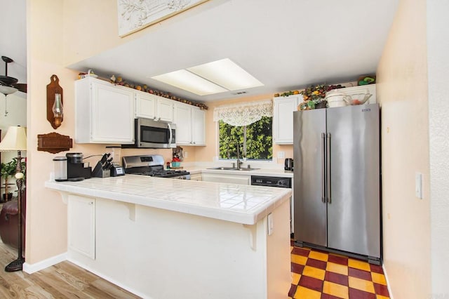 kitchen featuring stainless steel appliances, a peninsula, a sink, white cabinets, and light floors