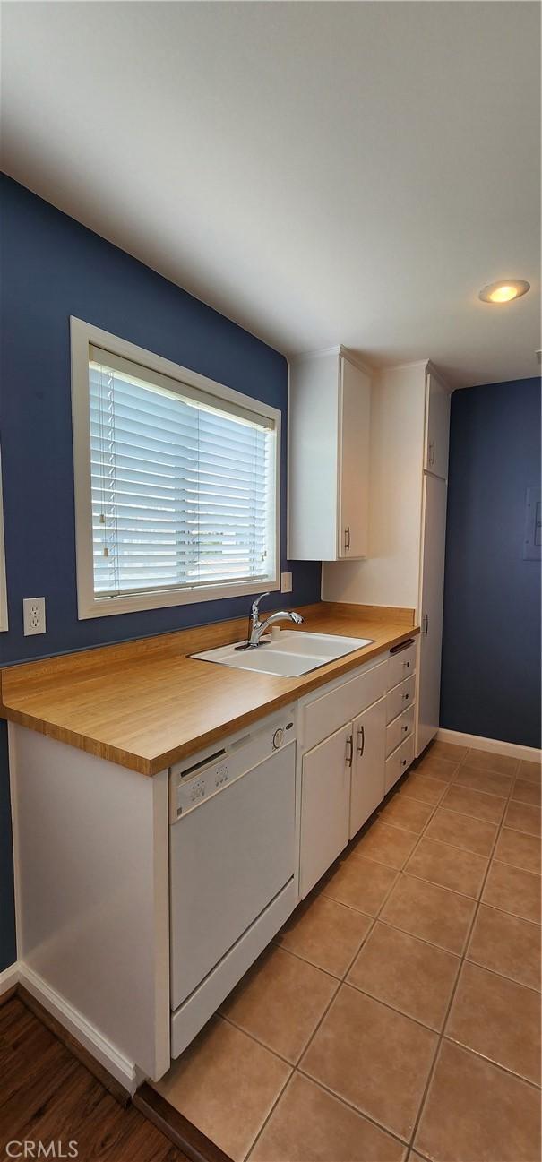 kitchen with light tile patterned floors, white dishwasher, a sink, and white cabinetry