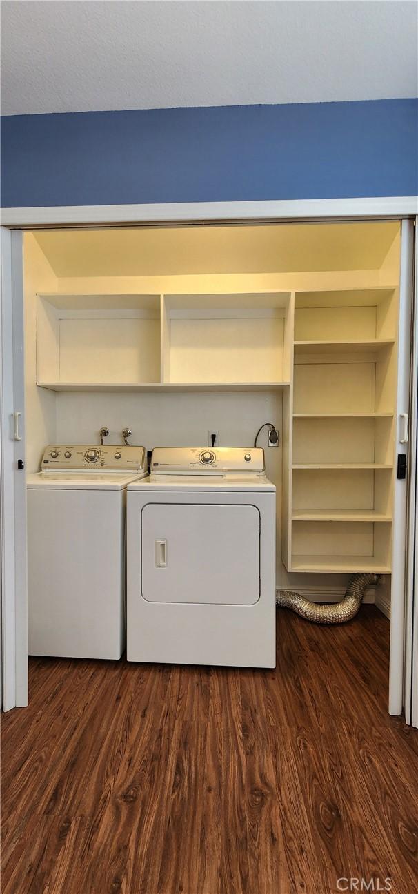 clothes washing area featuring dark wood-style floors, laundry area, and washing machine and clothes dryer