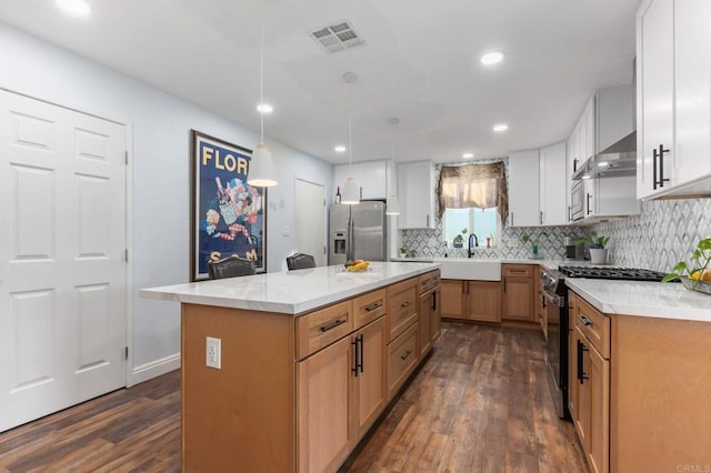 kitchen featuring dark wood finished floors, decorative backsplash, stainless steel appliances, wall chimney range hood, and a sink