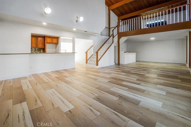 unfurnished living room with light wood-style floors, wood ceiling, stairs, and a high ceiling