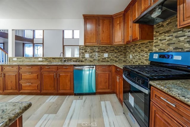 kitchen featuring stainless steel gas range oven, dishwasher, brown cabinets, under cabinet range hood, and a sink