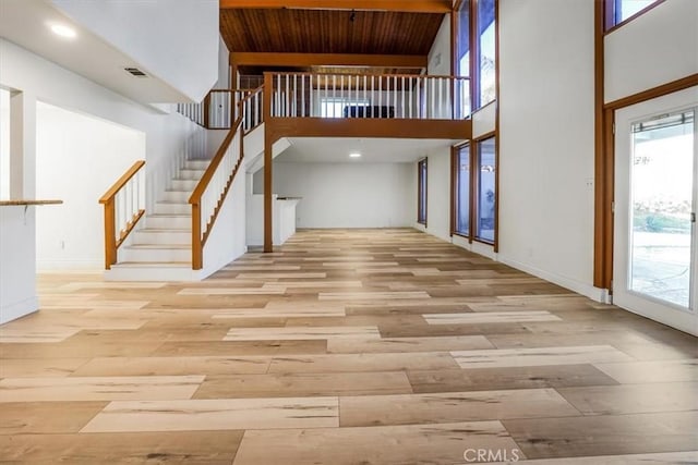 unfurnished living room featuring a towering ceiling, visible vents, stairway, and light wood finished floors