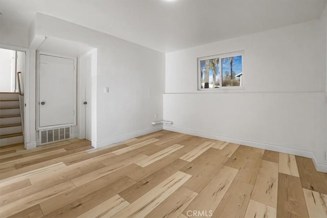 empty room featuring light wood-style floors, baseboards, stairs, and visible vents