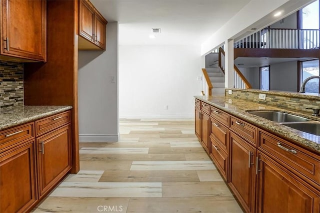 kitchen with light stone counters, a sink, visible vents, baseboards, and light wood finished floors