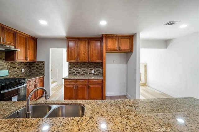 kitchen with light stone counters, under cabinet range hood, a sink, visible vents, and gas stove