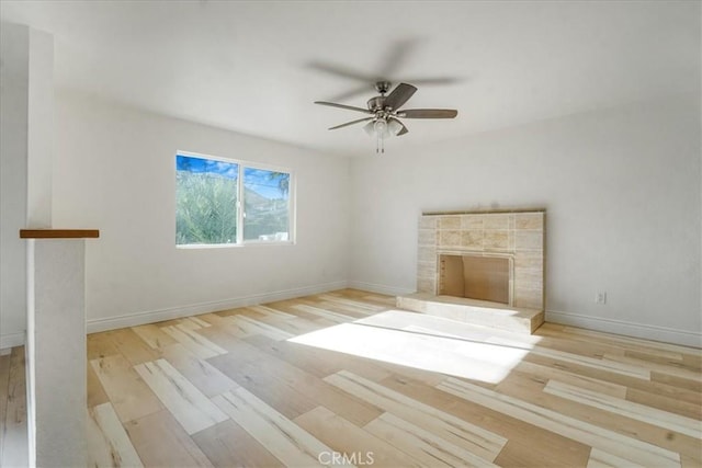 unfurnished living room with a ceiling fan, baseboards, a tiled fireplace, and wood finished floors