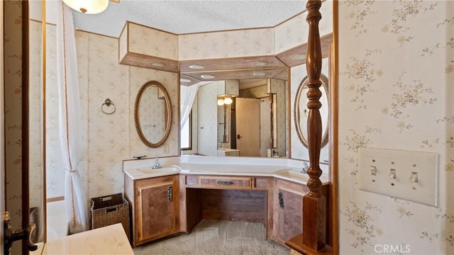 bathroom with a textured ceiling, vanity, and wallpapered walls