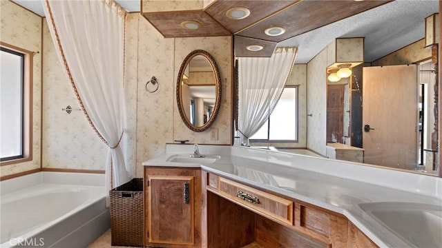 bathroom with a bath, wallpapered walls, double vanity, and a sink