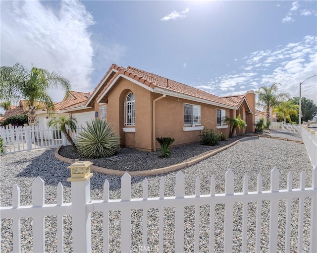 view of home's exterior with a fenced front yard, an attached garage, a tile roof, and stucco siding