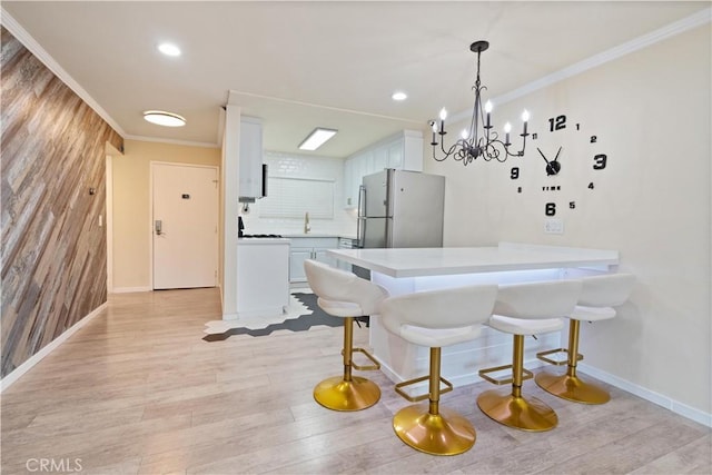 kitchen featuring light countertops, a peninsula, freestanding refrigerator, and crown molding