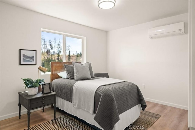 bedroom featuring an AC wall unit, light wood-type flooring, and baseboards