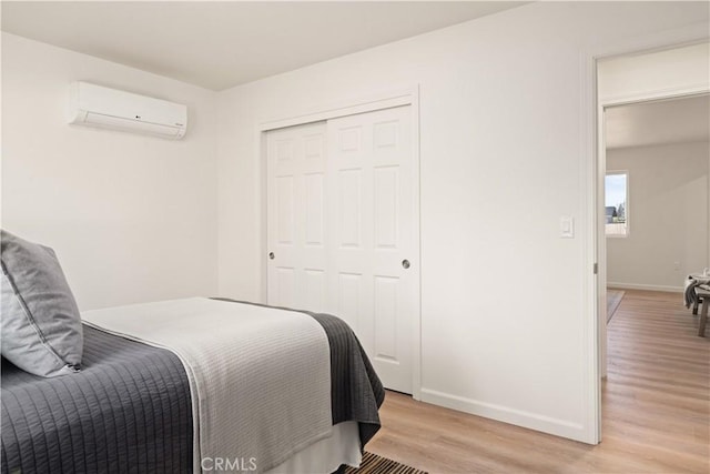 bedroom with light wood-type flooring, a closet, baseboards, and an AC wall unit