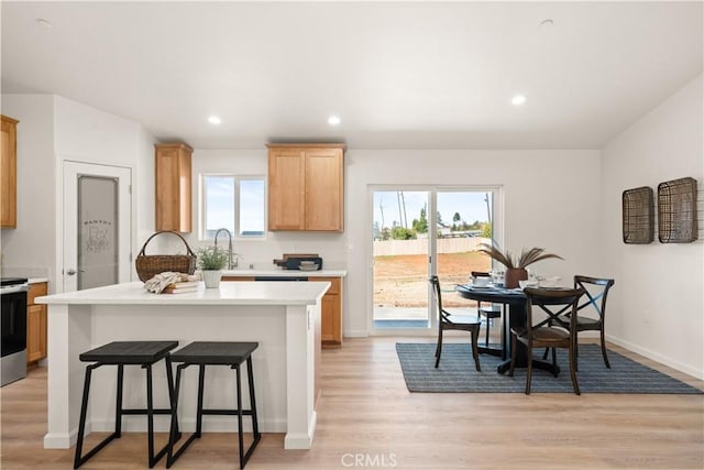 kitchen with a breakfast bar, a center island, light wood finished floors, recessed lighting, and light countertops