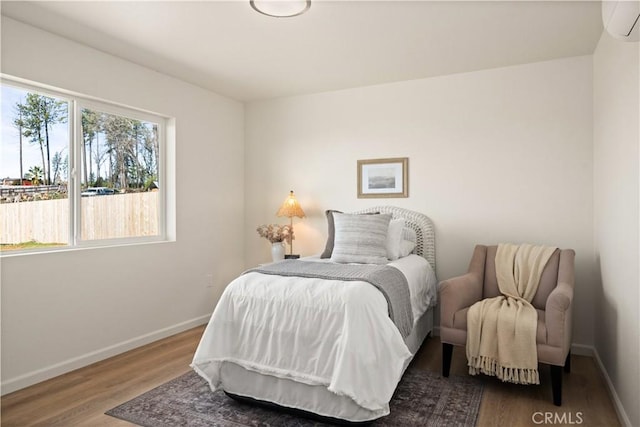 bedroom featuring a wall mounted air conditioner, baseboards, and wood finished floors