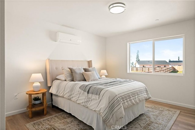 bedroom featuring a wall mounted air conditioner, baseboards, and wood finished floors