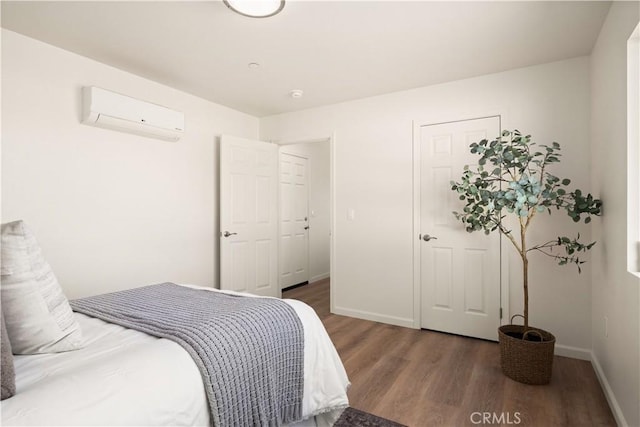 bedroom featuring a wall unit AC, baseboards, and wood finished floors