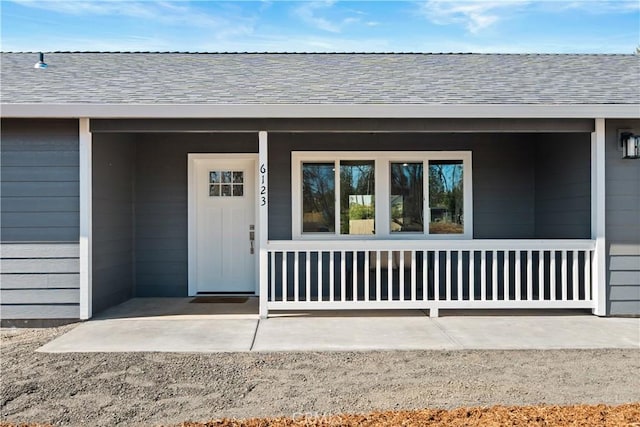 view of exterior entry with a porch and roof with shingles