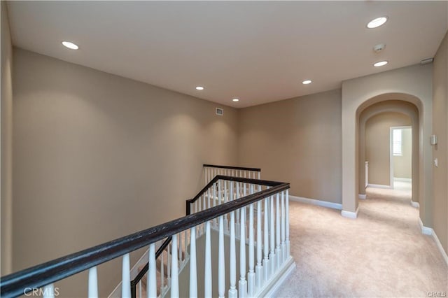 hall featuring arched walkways, recessed lighting, light colored carpet, an upstairs landing, and baseboards