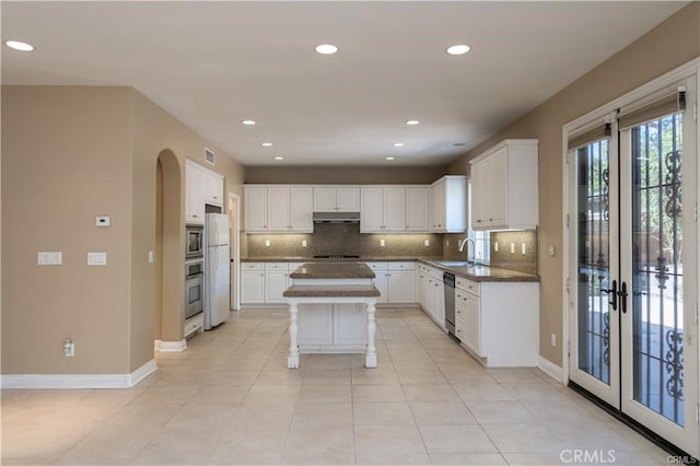 kitchen with stainless steel appliances, decorative backsplash, white cabinetry, and under cabinet range hood