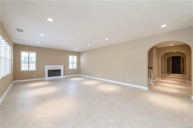 unfurnished living room with recessed lighting, arched walkways, baseboards, and a glass covered fireplace