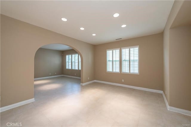 empty room with arched walkways, visible vents, baseboards, and recessed lighting