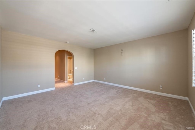 carpeted spare room featuring baseboards and arched walkways