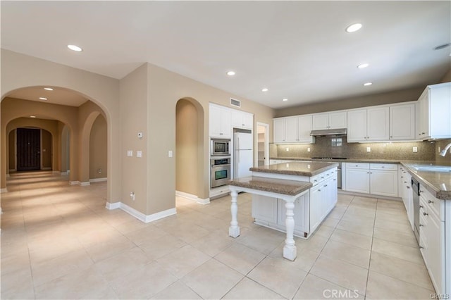 kitchen with decorative backsplash, a kitchen island, stainless steel appliances, under cabinet range hood, and a sink