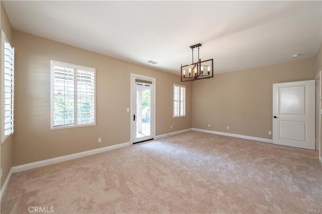 carpeted empty room featuring baseboards and a chandelier