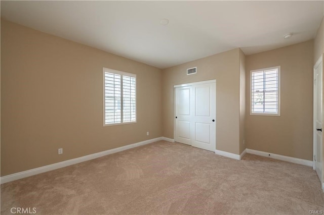 unfurnished bedroom featuring light colored carpet, visible vents, baseboards, and multiple windows