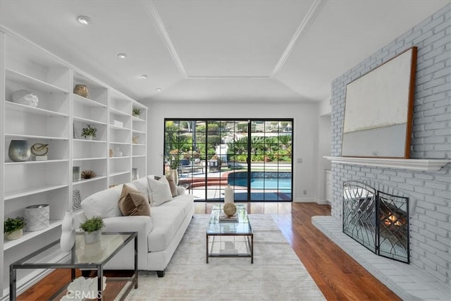 living area with wood finished floors, a brick fireplace, and a tray ceiling