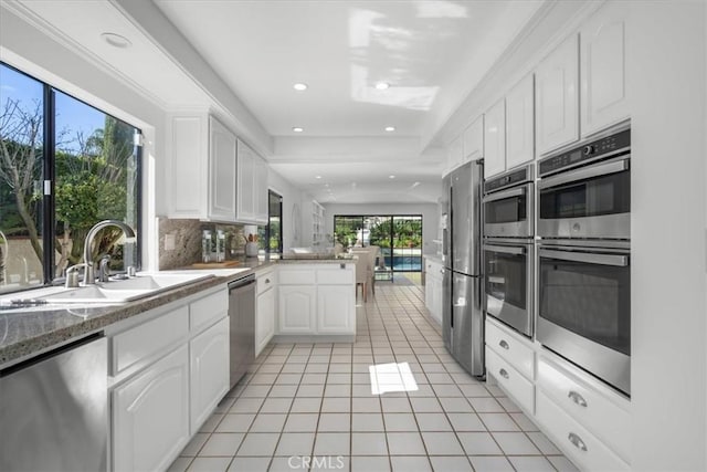 kitchen with white cabinetry, a sink, stainless steel appliances, light tile patterned flooring, and a peninsula