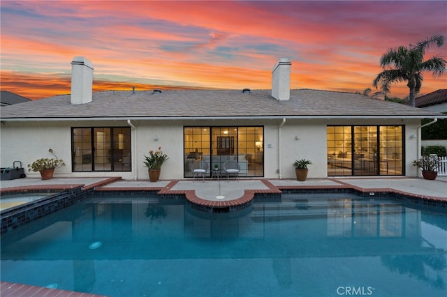 rear view of property featuring an outdoor pool, a chimney, and an in ground hot tub
