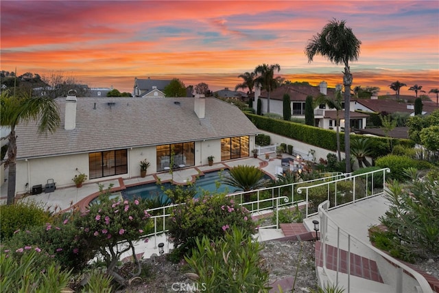 back of property at dusk with fence, a chimney, a patio, and a fenced in pool
